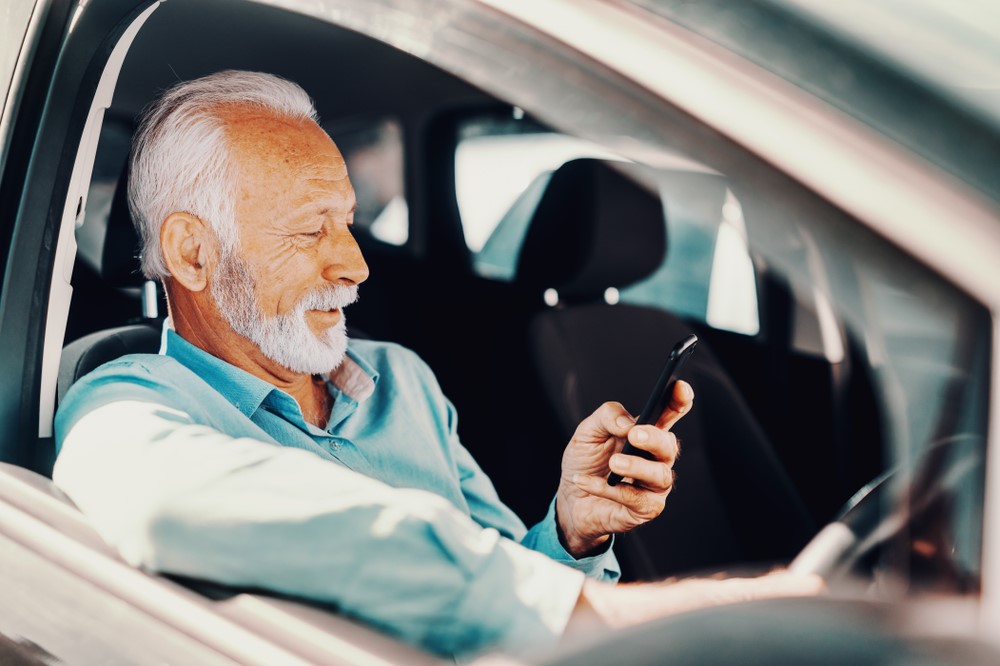 Old man looking at his phone in the car
